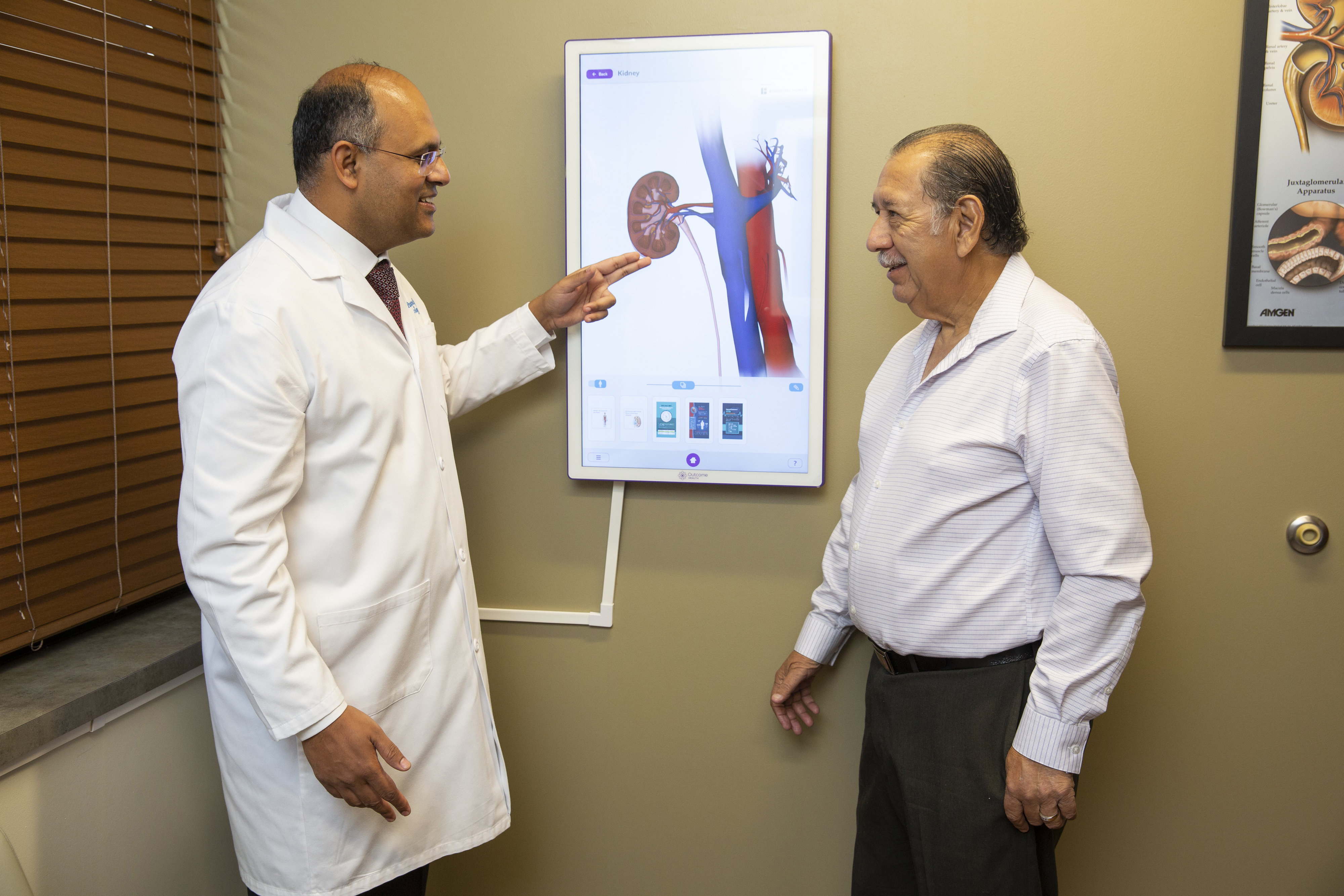 Male doctor on the left speaking with a male patient on the right, pointing to a kidney diagram on the wall.