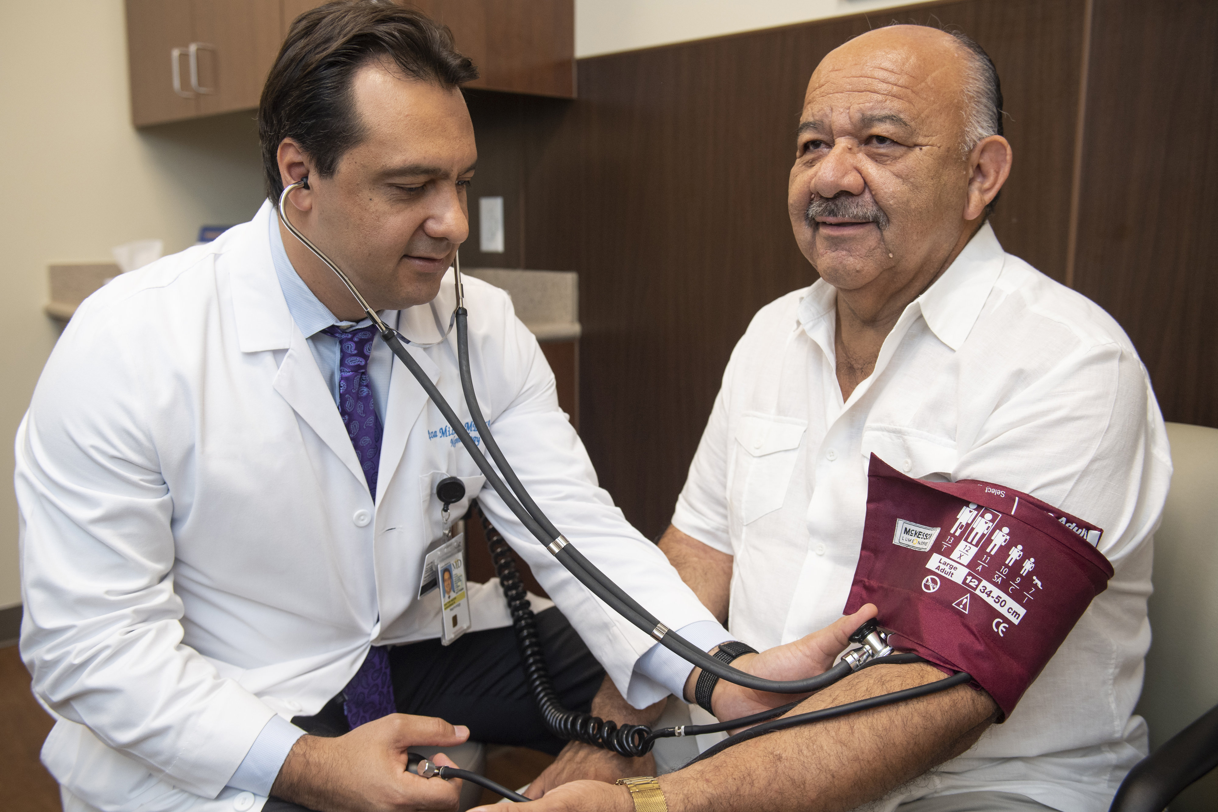 Male doctor checking a male patient's blood pressure with a cuff and stethoscope.